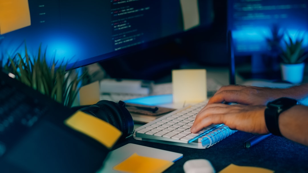 Programmer workspace night coding monitor keyboard sticky notes. Close-up of developer hands typing on keyboard in dark office with source code on screen